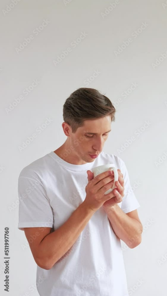 Refreshing coffee. Good morning. Enjoying life. Handsome man holding cup blowing on hot beverage smiling isolated on white vertical. Refreshing coffee. Good morning. Enjoying life. Handsome man holding cup blowing on hot beverage smiling isolated on white vertical.