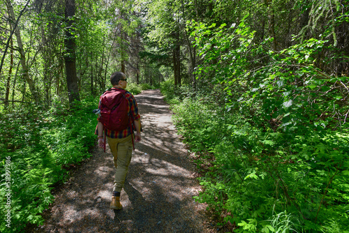 A young man with a red backpack hiking a wooded trail in Chugach National Forest, Alaska.
