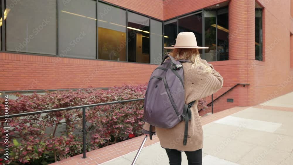 Back view of a female backpacker traveling around downtown in a big city. Tired traveler strolling along high street with modern architecture. High quality 4k footage Back view of a female backpacker traveling around downtown in a big city. Tired traveler strolling along high street with modern architecture. High quality 4k footage
