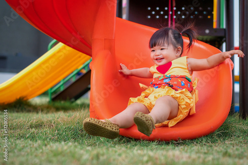 Asian cute baby playing on a slide at playground. 1 year 6 month baby enjoy and laugh at playground use as concept of play, health, mood and motion of baby and kid development.