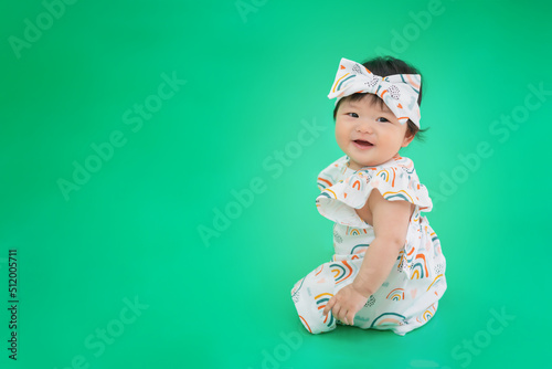 Asian happy cute baby smiling, sitting on green background. 6 months baby with copy space as concept of bedroom, development, health, mood and motion of baby and kid department in hospital