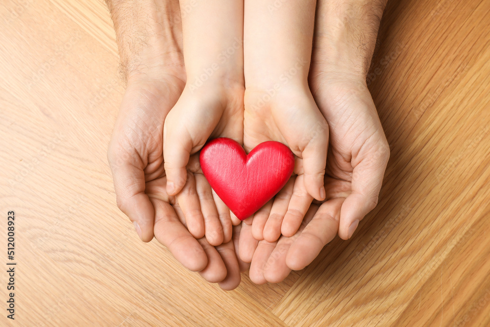 Fototapeta premium Man and kid holding red heart in hands at wooden table, top view