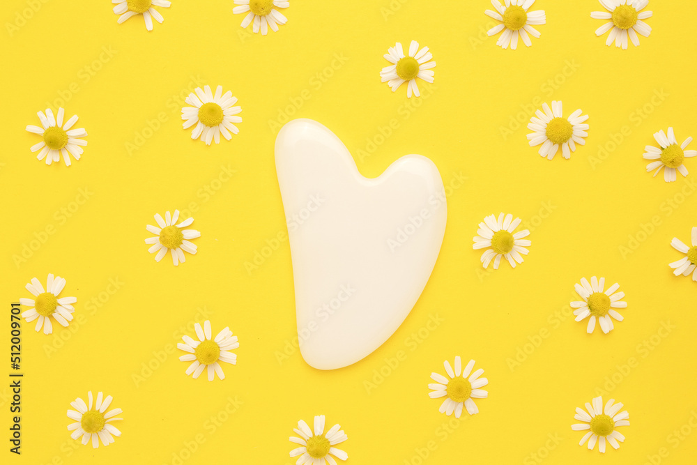 Gua sha stone for face massage. Chamomile flowers on yellow background. Face and body care spa concept.