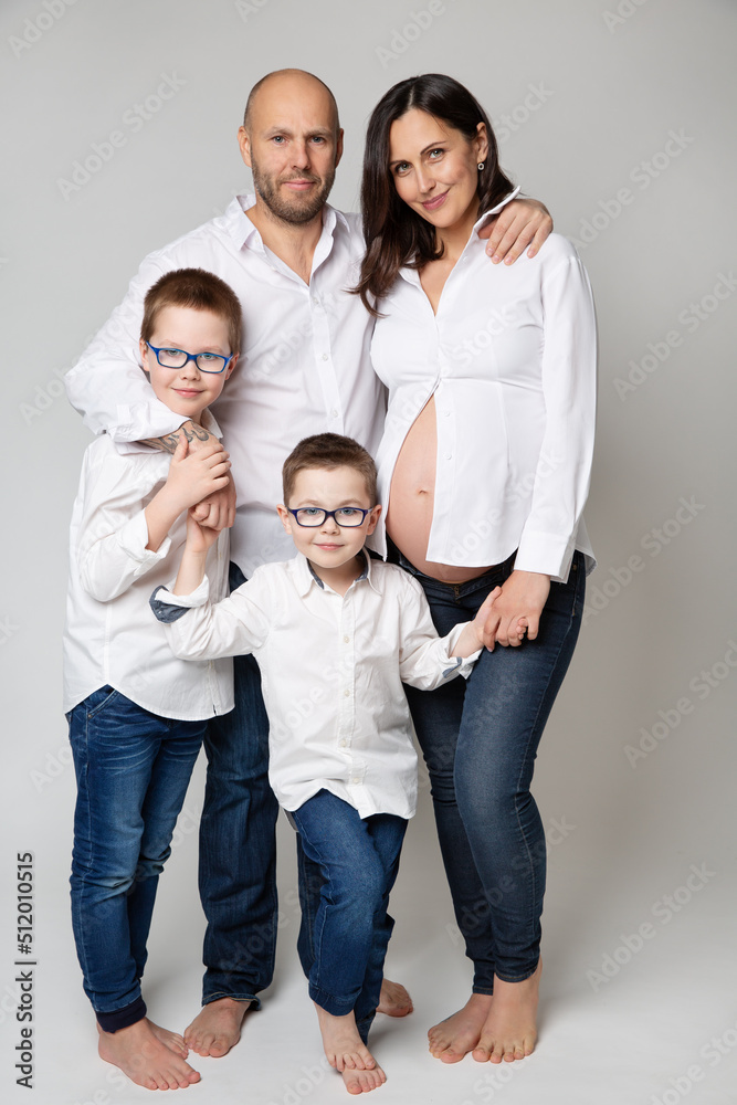 Family with Children over White background. Father and Pregnant Mother with Kids happy smiling embracing together. Parents and two Sons looking at camera standing over Gray