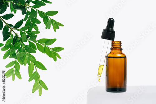 Natural medicine or aroma oil or beauty essence concept mockup vial with dropper with droplet on glass stand with green plant and white background. Face and body spa serum care concept banner