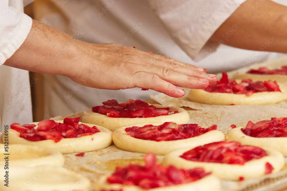 Baker makes filled pies from yeast dough, filling pies with strawberries. Work in bakery. Selective focus.
