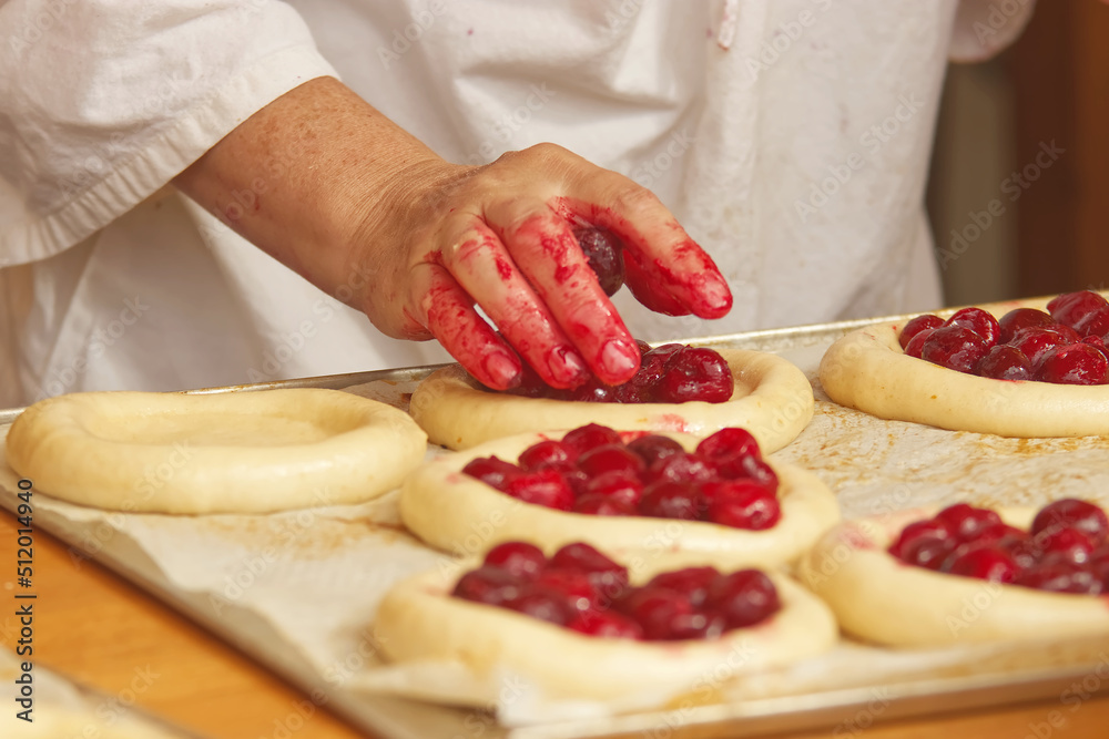 Baker makes filled pies from yeast dough, filling pies with cherries. Work in bakery. Selective focus.