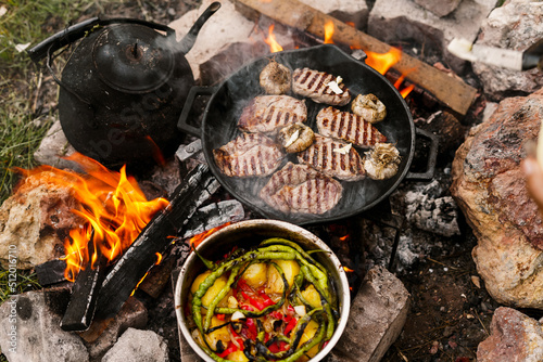 Campfire red meat in pan, near the fire outdoors. bushcraft, adventure, tea, knife and camping concept
