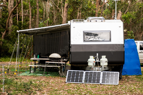 RV caravan camper on a campsite in the bush forest nature. Awning, portable toilet, solar panels, bbq, table. Family camping photo