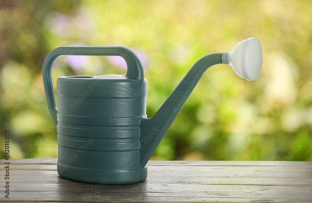 Watering can on wooden table outdoors Watering can on wooden table outdoors