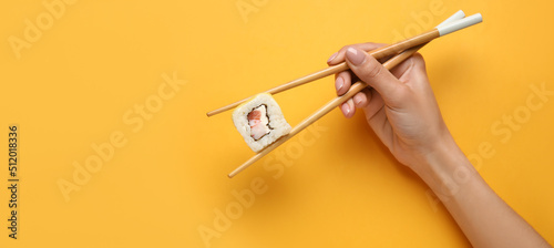 Hand holding chopsticks with delicious sushi roll on yellow background with space for text