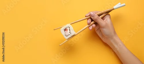 Obraz  z motywem Hand holding chopsticks with delicious sushi roll on yellow background with space for text