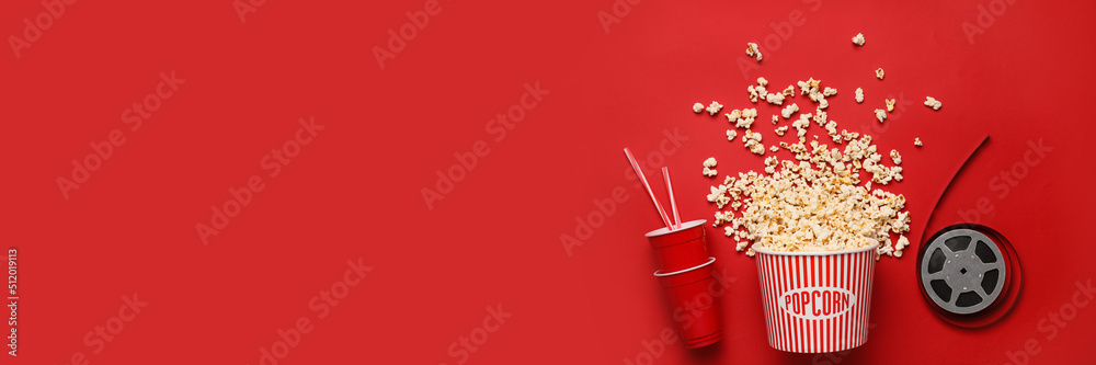 Bucket with popcorn, cups and film reel on red background with space for text Bucket with popcorn, cups and film reel on red background with space for text