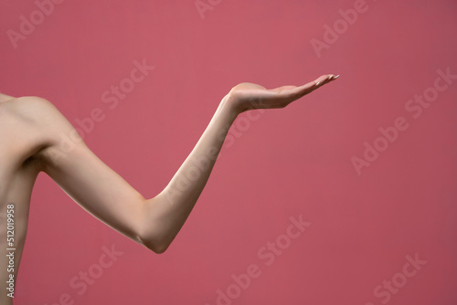 Young woman's stretched skinny arm and open palm holding imaginary product. Isolated on pink background © vladimirfloyd