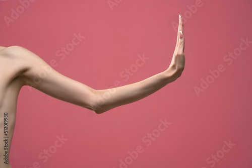Young woman's stretched skinny arm with stop gesture. Isolated on pink background © vladimirfloyd