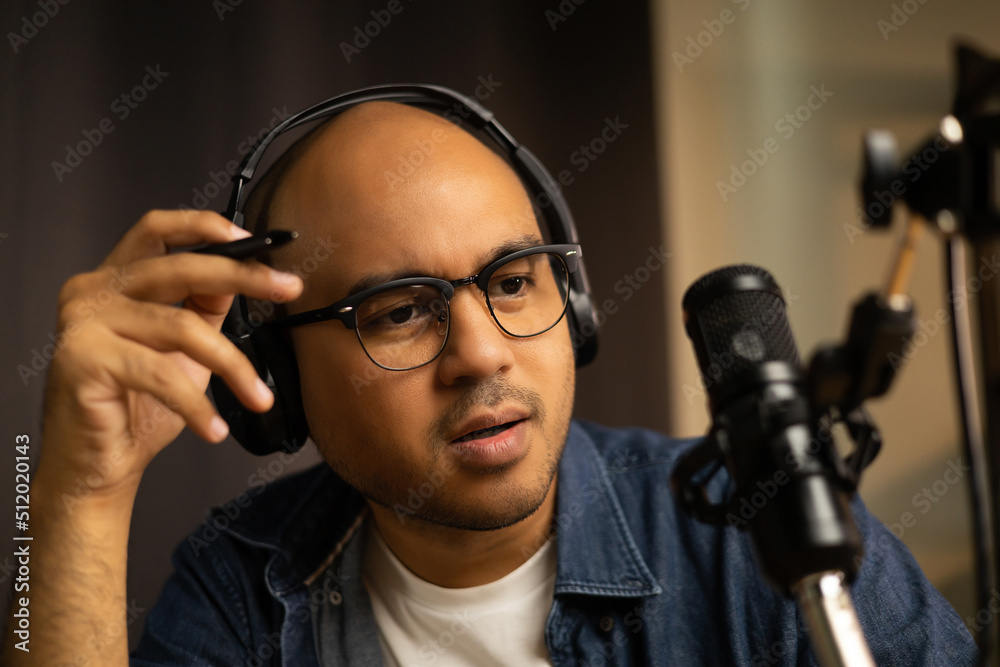 Young asian man host streaming podcast with condenser microphone work on laptop at small broadcast home studio. Content creator blogger recording voice over radio interview guest conversation Young asian man host streaming podcast with condenser microphone work on laptop at small broadcast home studio. Content creator blogger recording voice over radio interview guest conversation