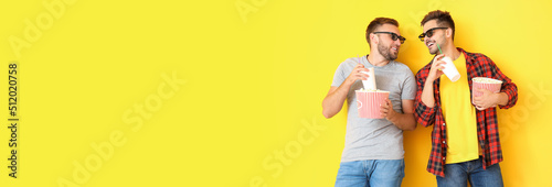 Young men with popcorn and drinks watching movie on yellow background with space for text © Pixel-Shot