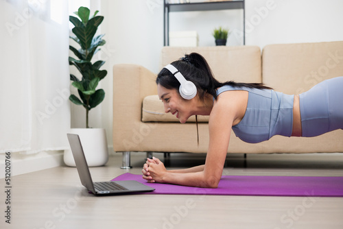 Young asian woman doing planking workout exercise on yoga mat. Body weight training for health strength and powerful. Female Bodybuilder and muscle physical at home. Looking yoga lesson on laptop