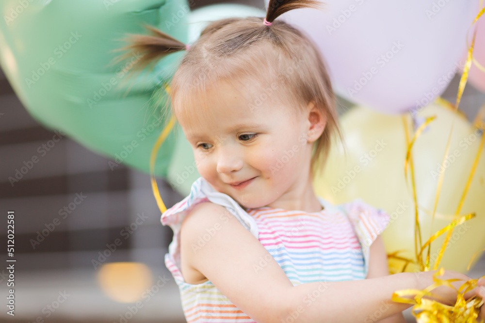 Funny girl child toddler with two tails with balloons outside. Balloons of pastel delicate colors Funny girl child toddler with two tails with balloons outside. Balloons of pastel delicate colors