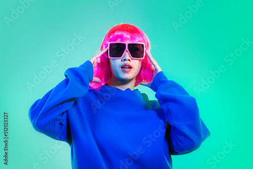 Young asian woman in blue sweatshirt pink short hair punk style wearing sunglasses posing dancing on the green screen background.