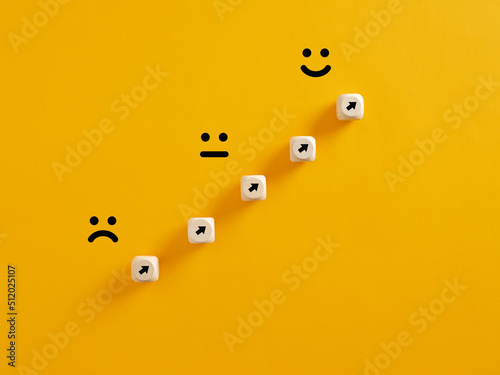 Arrows on wooden cubes pointing from a sad expression towards a happy one. Personal growth and aspiration