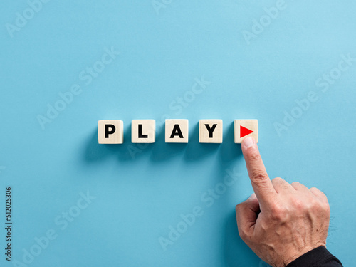 Male hand presses the play button with the word play on wooden cubes.