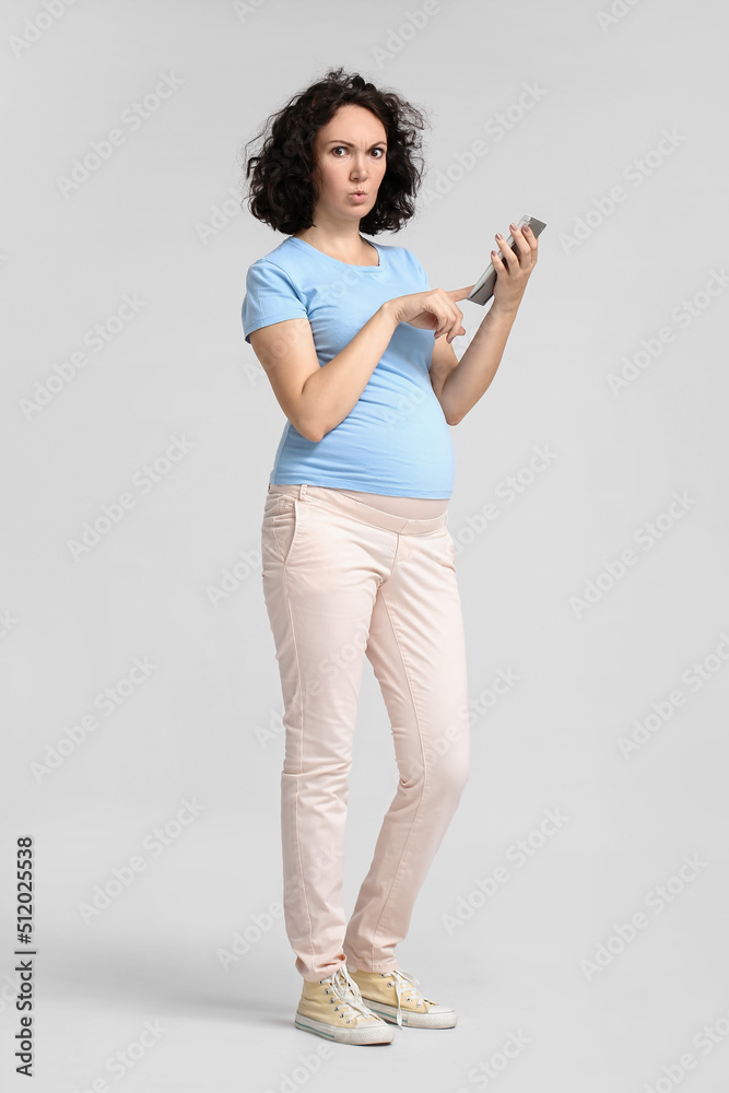 Upset young pregnant woman using calculator on light background Upset young pregnant woman using calculator on light background