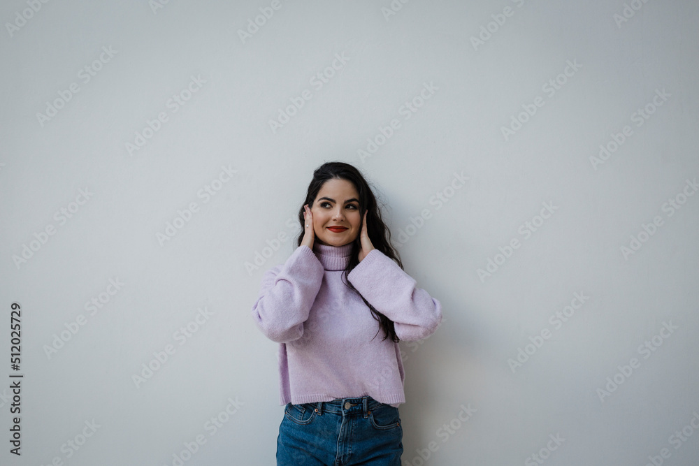 Smiling woman covering ears with hands in front of white wall Smiling woman covering ears with hands in front of white wall