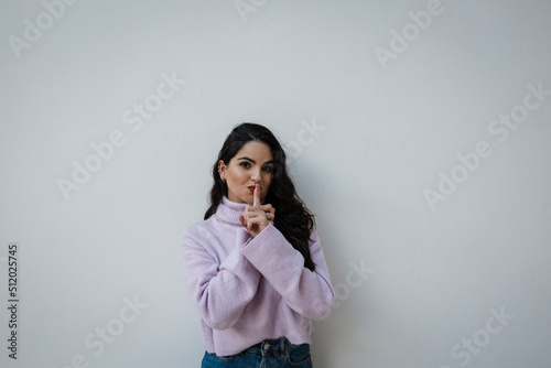 Beautiful woman gesturing with finger on lips in front of white wall