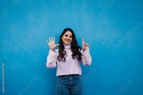 Smiling young beautiful woman showing number 6 in front of blue wall photo