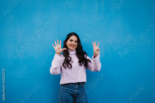 Smiling young beautiful woman showing number 8 in front of blue wall photo