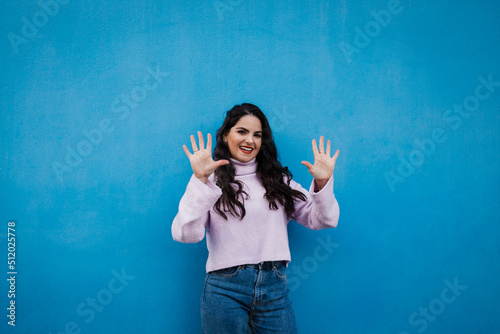Smiling young beautiful woman showing number 10 in front of blue wall photo