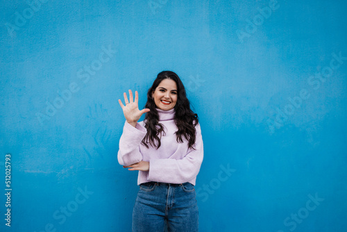 Smiling young beautiful woman showing number 5 in front of blue wall photo