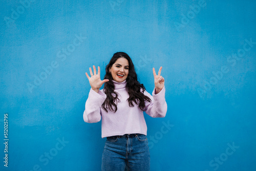 Smiling young beautiful woman showing number 7 in front of blue wall photo