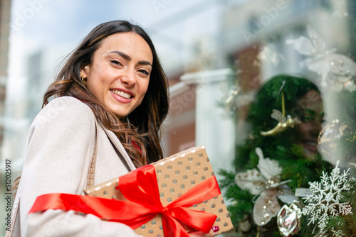 Happy woman with Christmas present standing by glass window