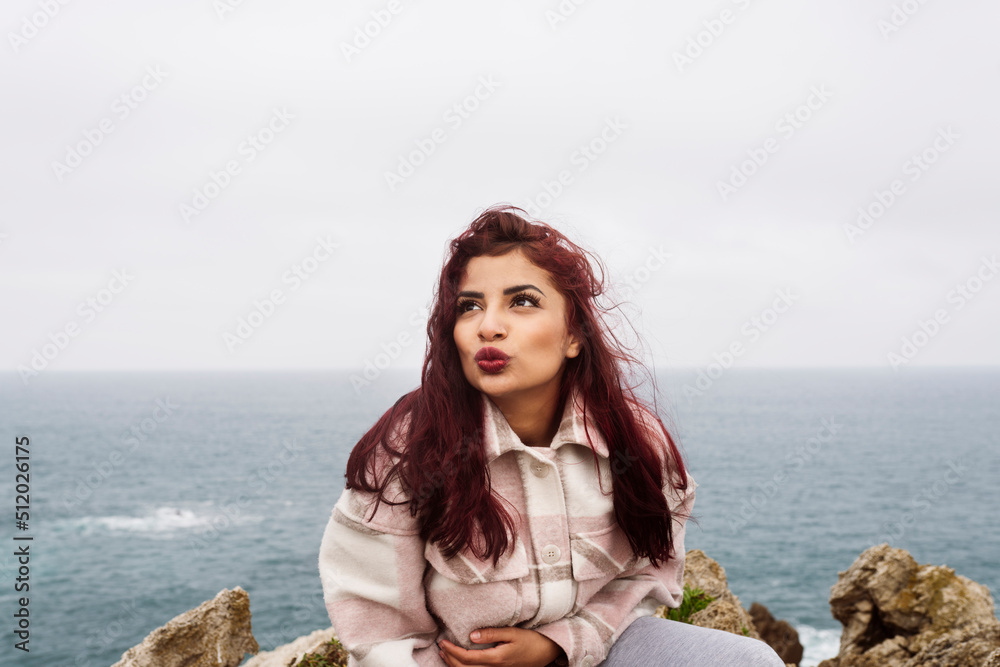 Woman with red hair puckering lips sitting on rock Woman with red hair puckering lips sitting on rock