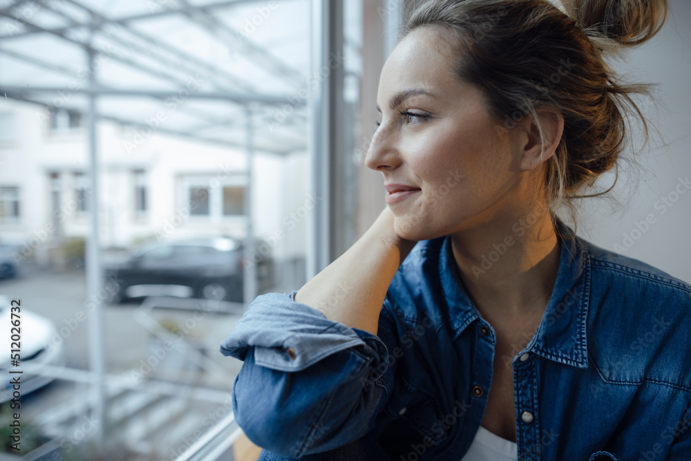 Thoughtful woman looking out through window at home Thoughtful woman looking out through window at home