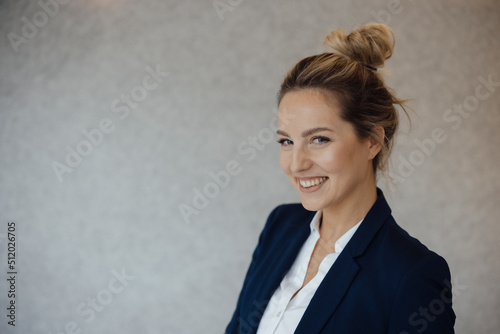 Happy businesswoman with blond hair bun in front of gray wall photo