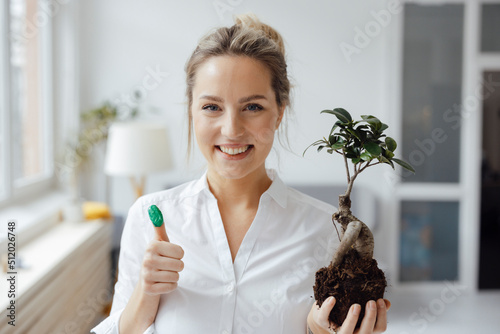 Smiling businesswoman holding plant showing green thumb in office photo