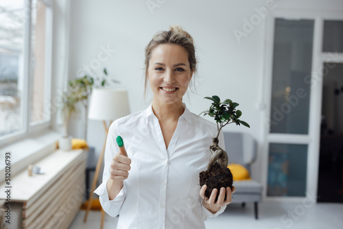 Happy businesswoman holding plant showing green thumb in office photo