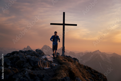 Hiker running on top of Sauling mountain peak with summit cross photo