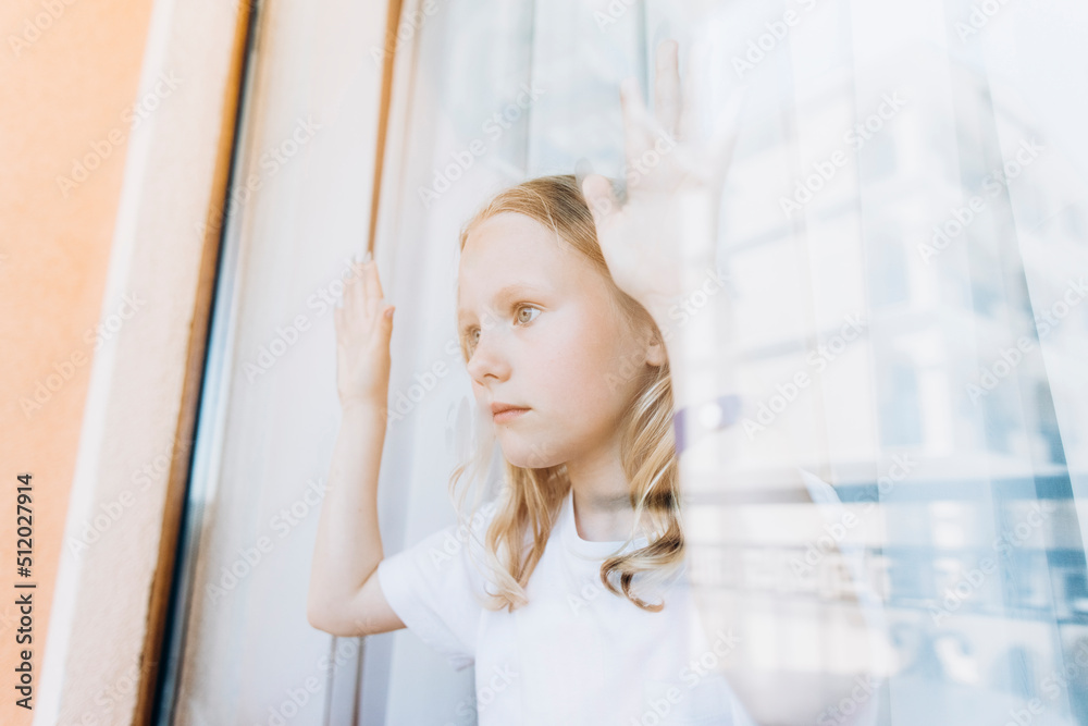 Contemplative girl looking through glass window at home Contemplative girl looking through glass window at home
