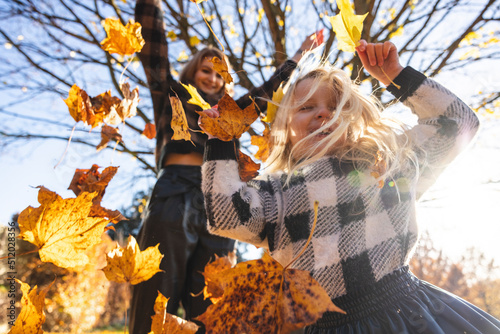 Mother throwing autumn leaves on daughter playing at park photo
