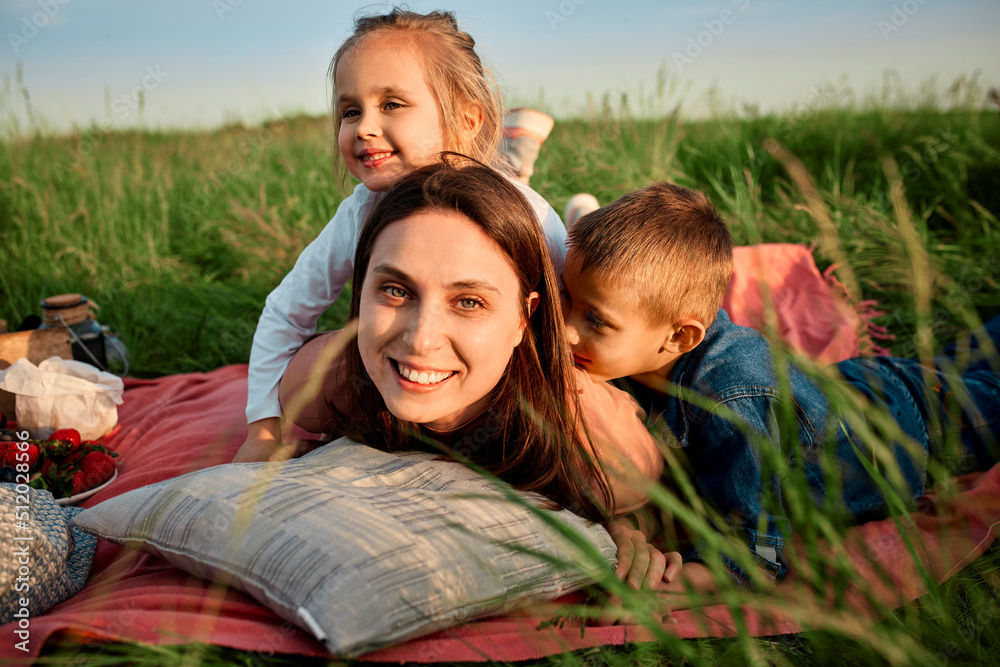 Smiling mother lying by children in picnic blanket at field Smiling mother lying by children in picnic blanket at field