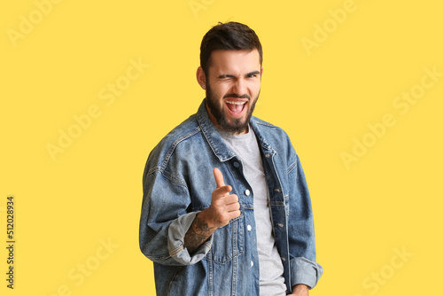 Slika na platnu Smiling man pointing at viewer and winking on yellow background