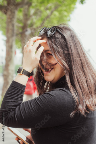 An image of a woman, smiling, while putting hair put of her face