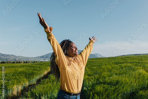 Happy young woman with arms raised in meadow