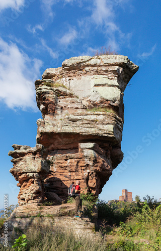 Germany, Rhineland-Palatinate, Senior hiker standing in front of sandstone rock formation in Palatinate Forest with Trifels Castle in distant background photo