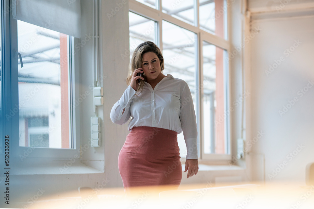 Confident plus size businesswoman talking on smart phone at work place Confident plus size businesswoman talking on smart phone at work place