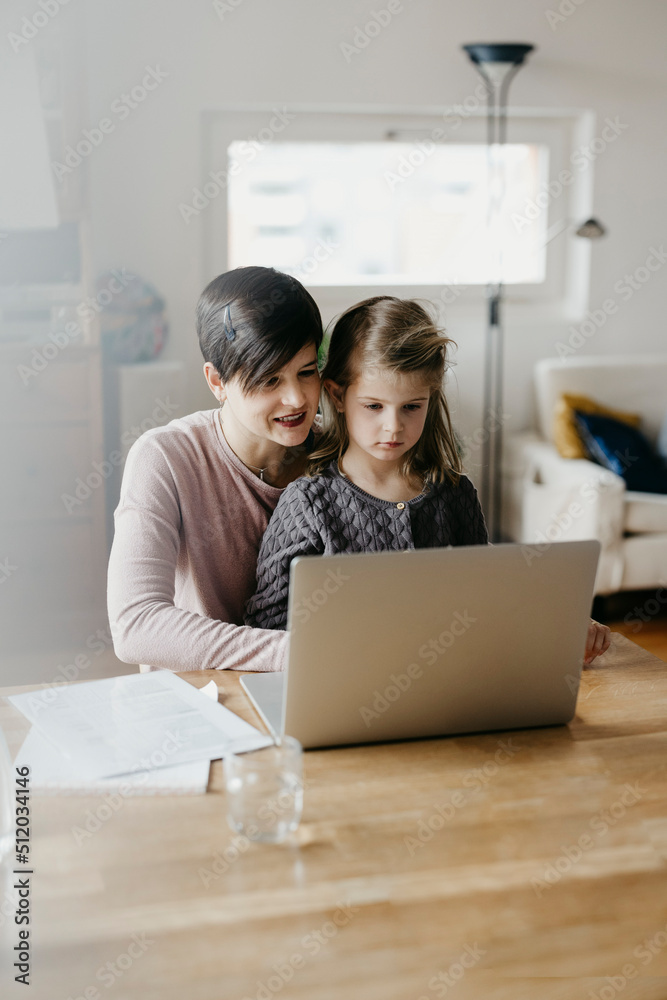 Mother and daughter watching laptop together at desk Mother and daughter watching laptop together at desk